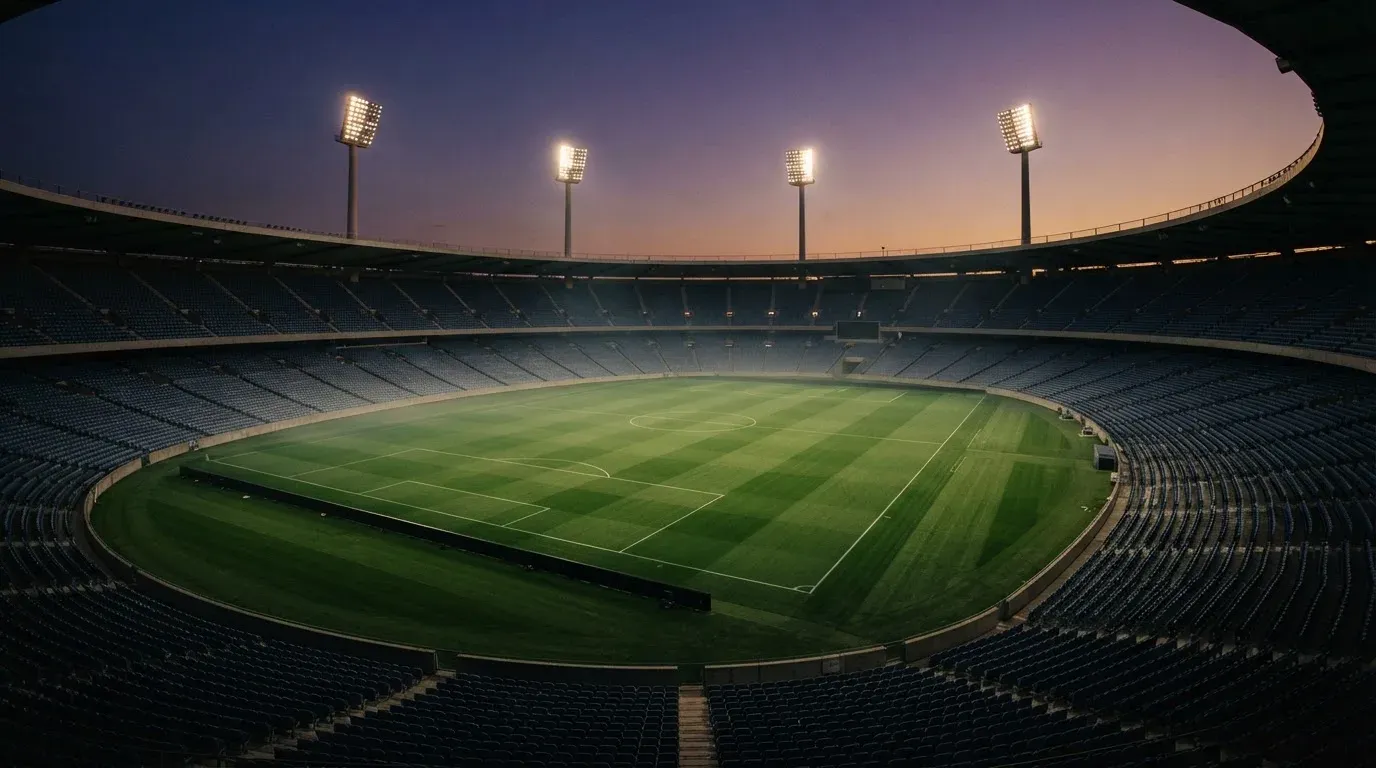 An empty football stadium with floodlight masts at dusk