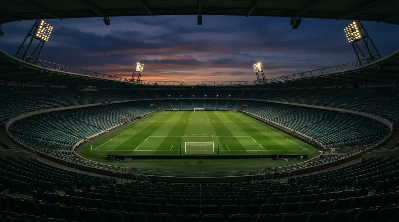 An empty football stadium with floodlight masts at dusk