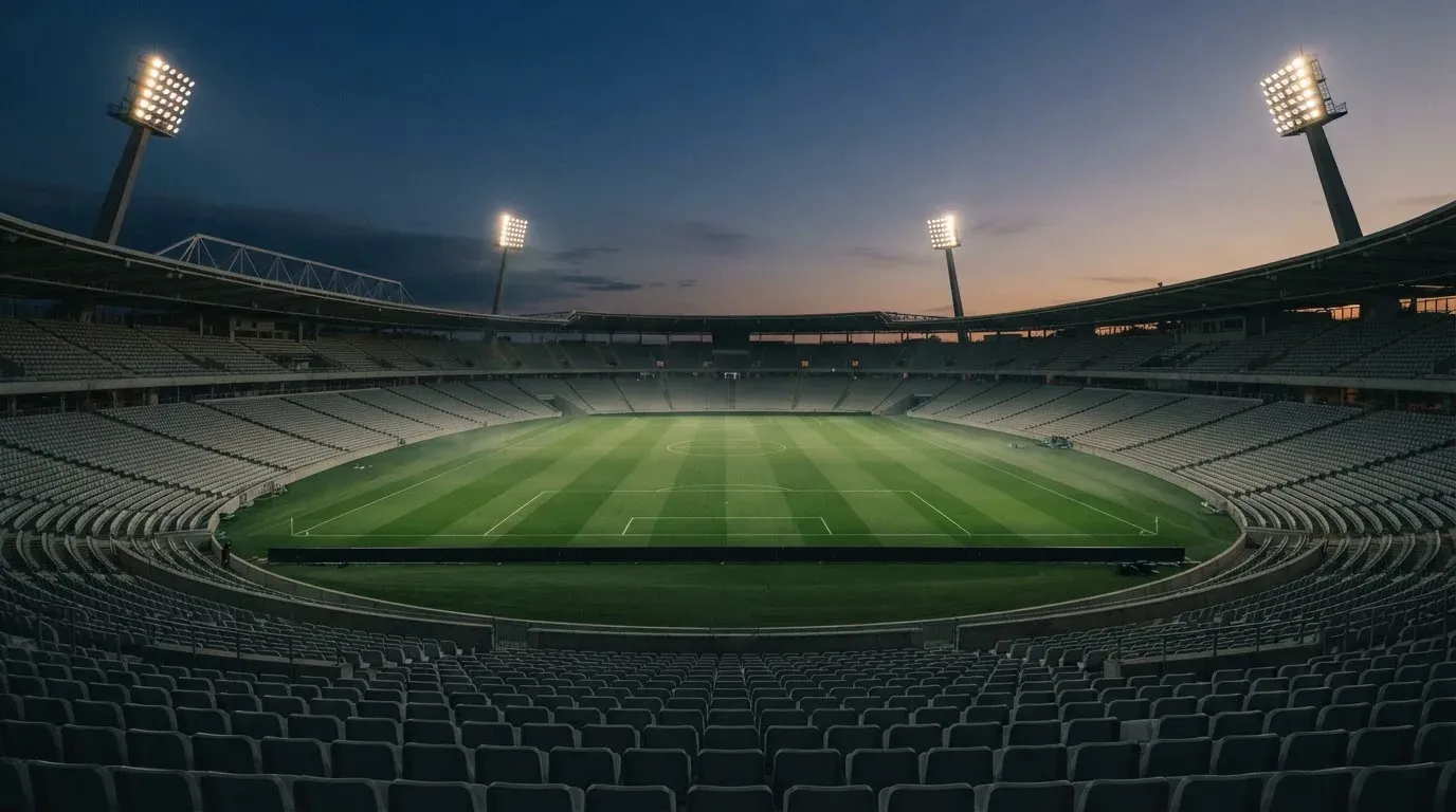 An empty football stadium with floodlight masts at dusk