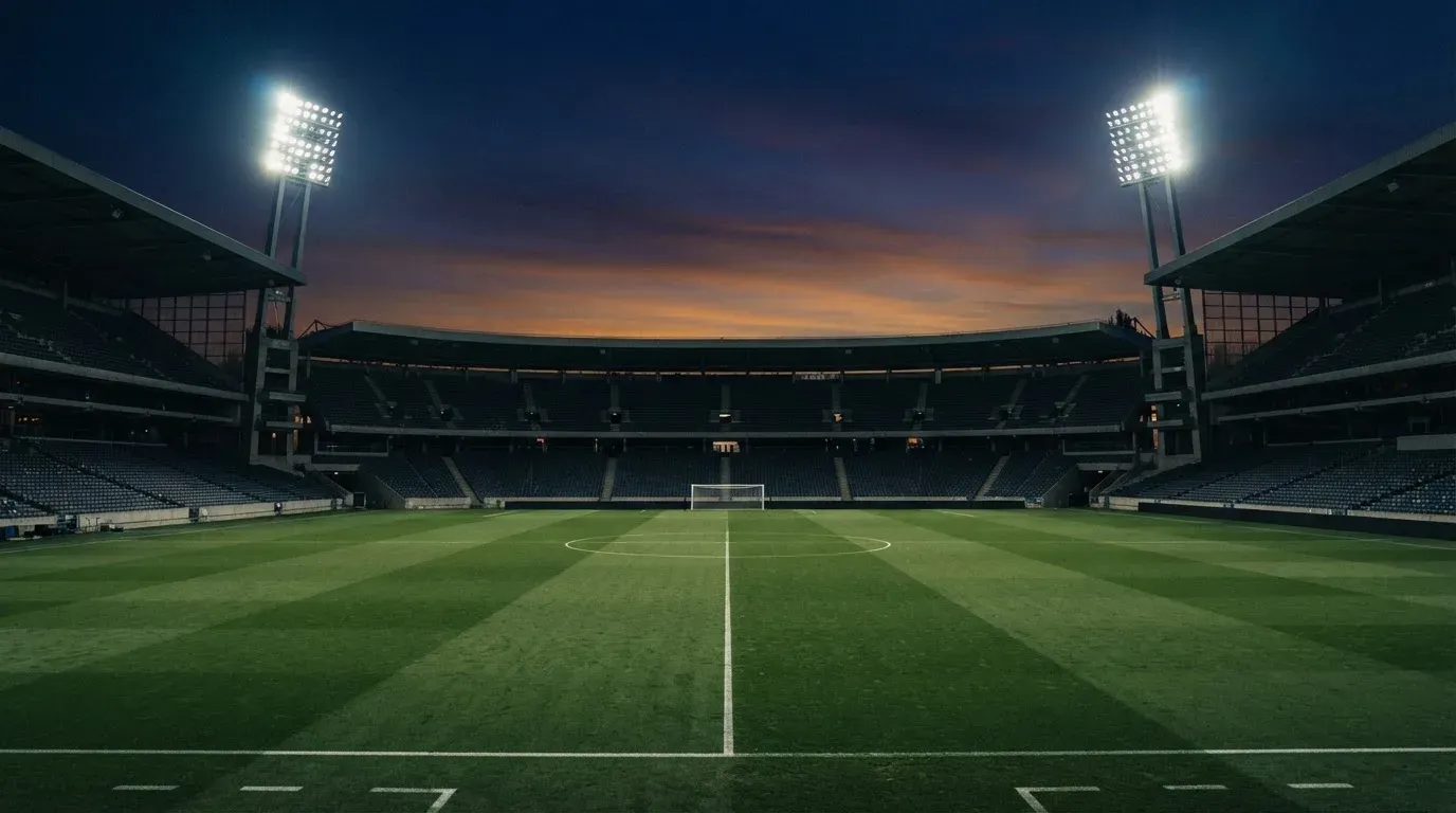 An empty football stadium with floodlight masts at dusk